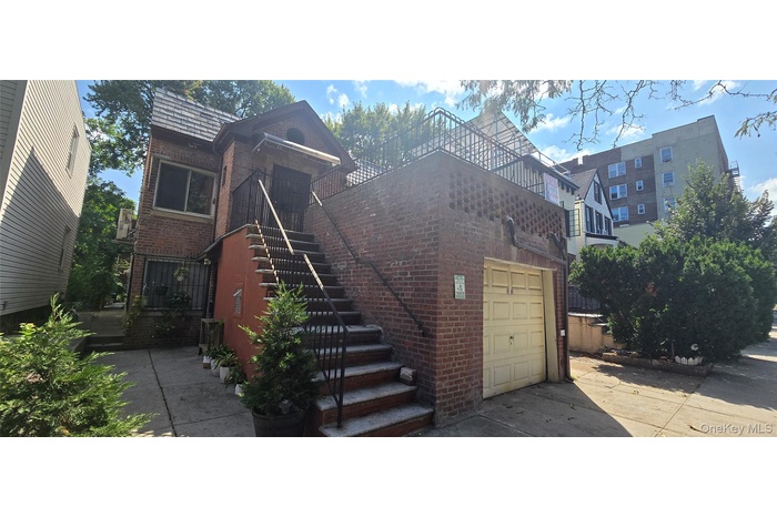front view of property featuring brick siding, stairs, an attached garage, concrete driveway, and a balcony