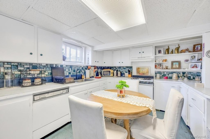 Kitchen with white cabinets, light countertops, white appliances, open shelves, and tasteful backsplash