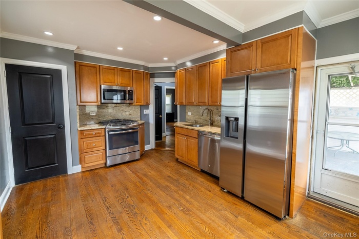 Kitchen featuring stainless steel appliances, ornamental molding, backsplash, light stone counters, and dark wood-type flooring