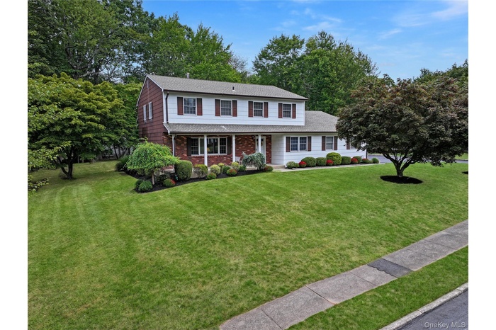Traditional-style house featuring brick siding, roof with shingles, a front lawn, and a porch
