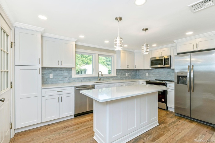 Kitchen with stainless steel appliances, light countertops, white cabinets, backsplash, and ornamental molding