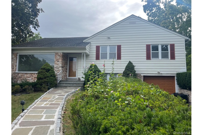 Split level home with stone siding, an attached garage, and a shingled roof
