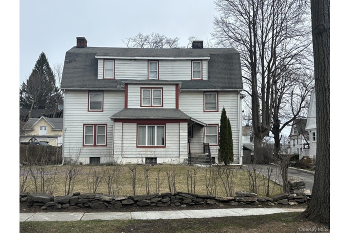 View of front facade with a chimney, a fenced front yard, roof with shingles, and a gambrel roof