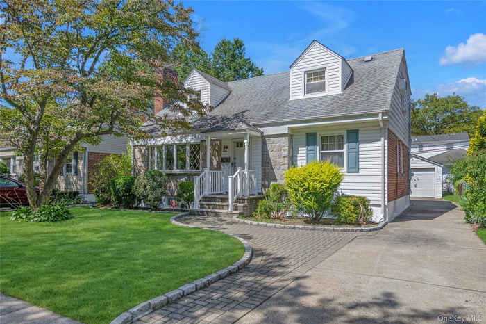 New england style home with an outbuilding, a front yard, a shingled roof, a porch, and a detached garage