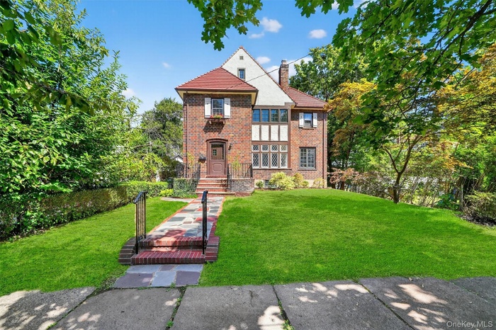 Tudor home with brick siding, a front lawn, and a chimney