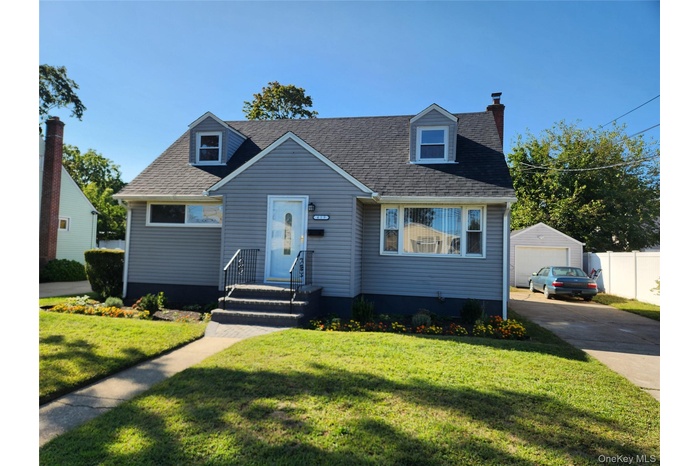 Cape cod-style house featuring a chimney, a front yard, a shingled roof, an outdoor structure, and a garage