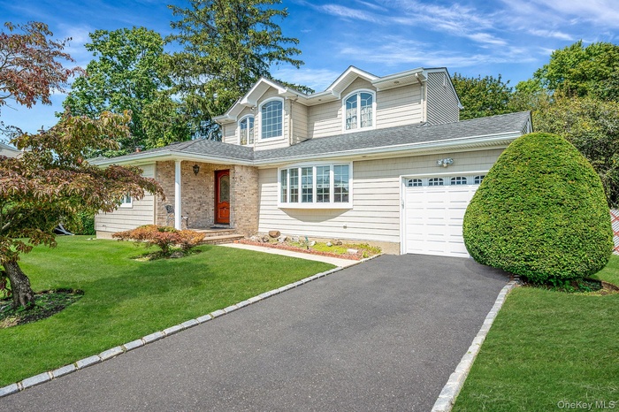 Traditional home featuring a front lawn, roof with shingles, driveway, an attached garage, and covered porch
