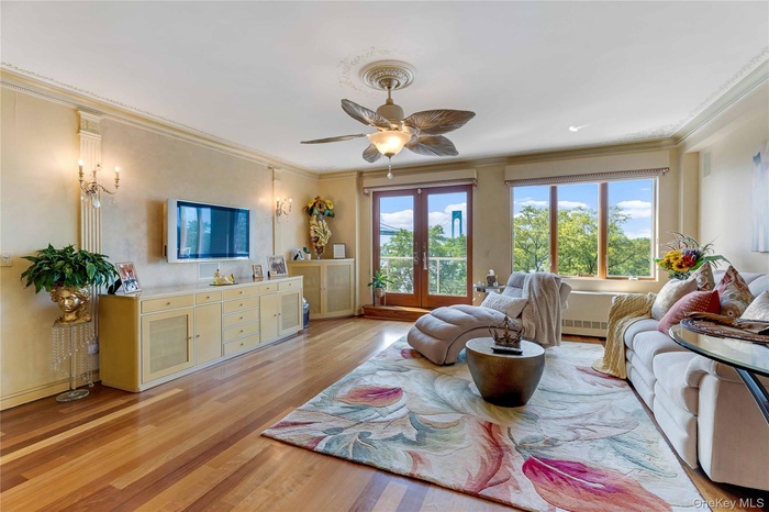 Living area with ornamental molding, plenty of natural light, light wood-style floors, a ceiling fan, and french doors