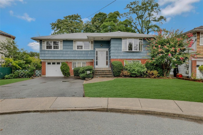 Raised ranch featuring brick siding, a front yard, driveway, and an attached garage