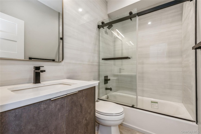 Full bath with bath / shower combo with glass door, vanity, and tile walls.The pictures represent the model unit.