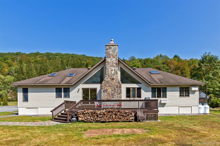 Back of house featuring a chimney, a deck, roof with shingles, and a yard