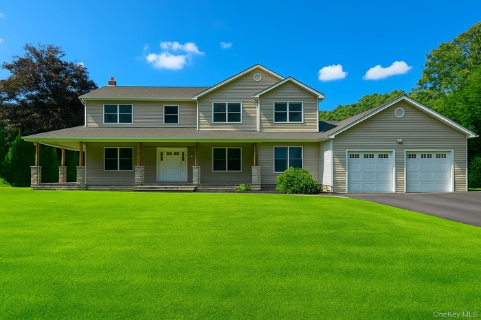 View of front facade with covered porch, asphalt driveway, a front yard, a chimney, and an attached garage