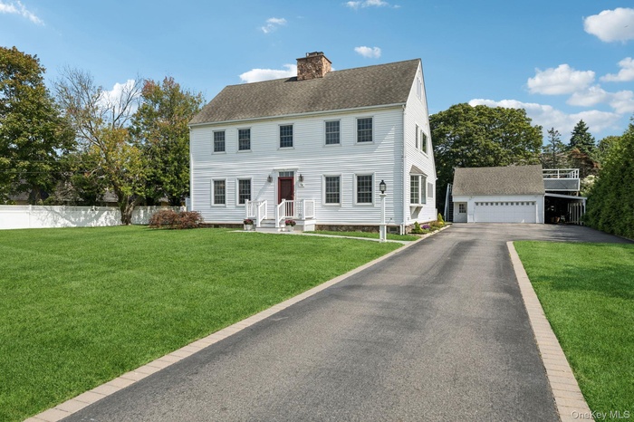 Colonial-style house featuring , a chimney, a front lawn, a shingled roof, and a detached garage