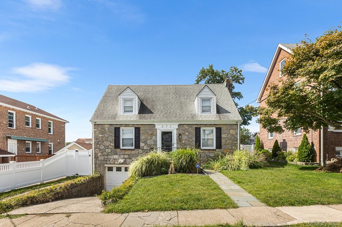 New england style home featuring stone siding, roof with shingles, a chimney, and a garage