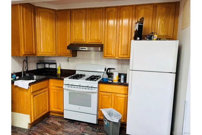 Kitchen featuring white appliances, under cabinet range hood, a sink, and brown cabinets