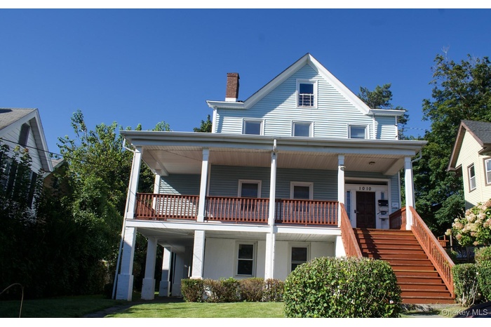View of front of home featuring covered porch, a chimney, stairs, and a front lawn