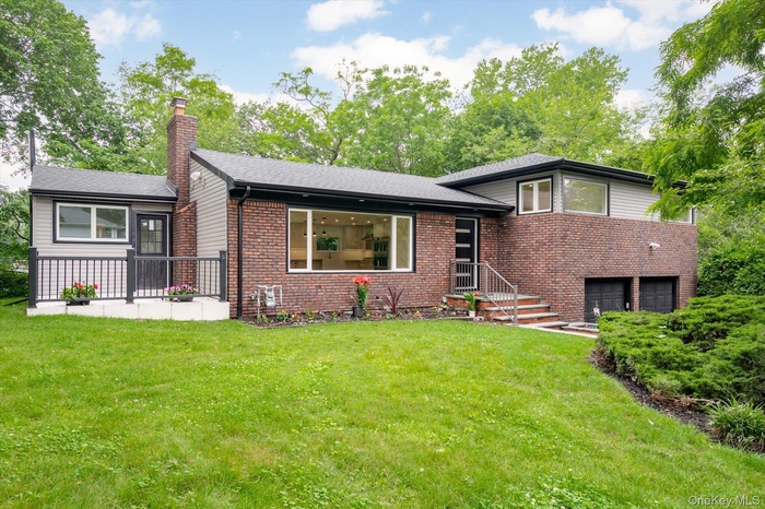 Split level home featuring a chimney, a garage, a front lawn, and brick siding