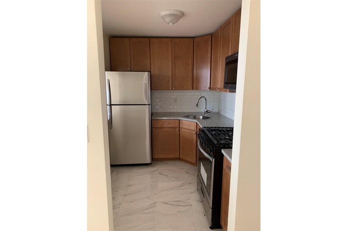 Kitchen featuring paneled fridge, stove, light marble finish flooring, brown cabinets, and backsplash