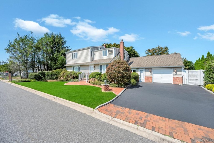 View of front facade with asphalt driveway, an attached garage, brick siding, a chimney, and a gate