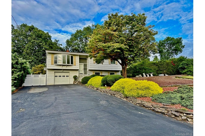 Bi-level home with driveway, a garage, a chimney, and view of scattered trees