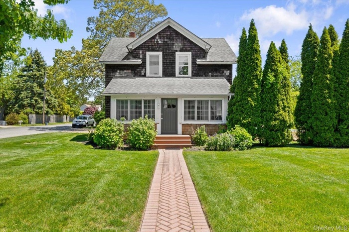 View of front of house with roof with shingles, a front lawn, and covered porch