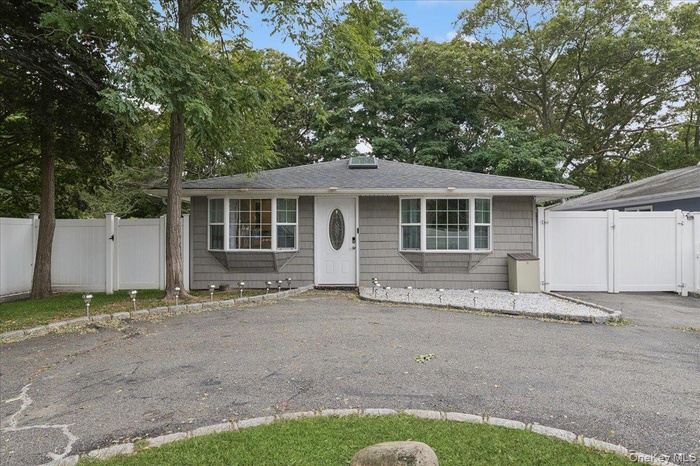 View of front of house with a gate, a shingled roof, and view of wooded area