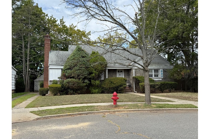 View of front of house featuring a front yard, a chimney, roof with shingles, and stone siding