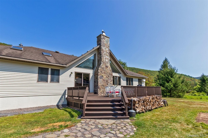 Back of property with a chimney, a yard, a deck, and roof with shingles