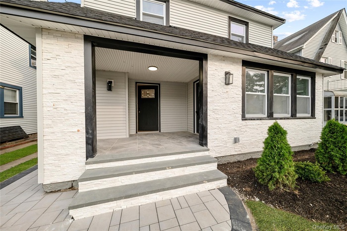 View of exterior entry featuring roof with shingles, covered porch, and brick siding