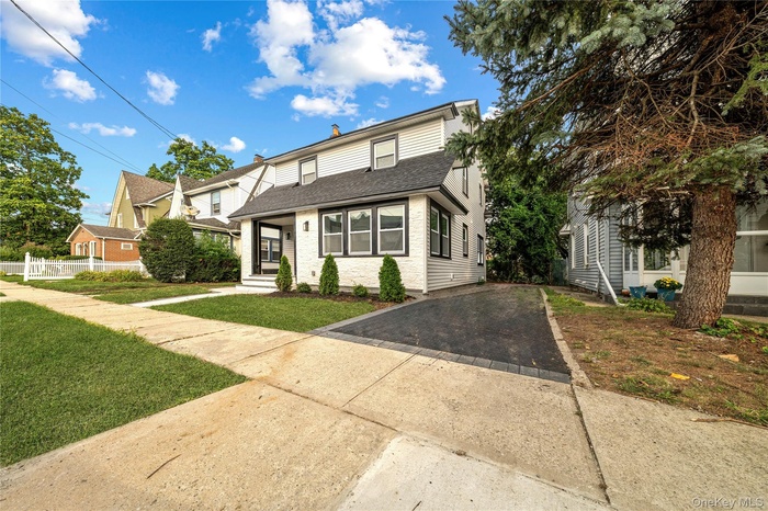 View of front facade featuring a shingled roof, asphalt driveway, and a front yard