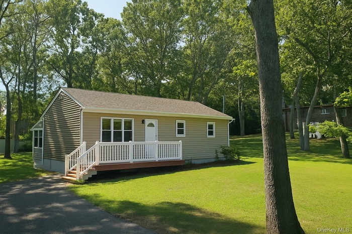View of front of house featuring a wooden deck, view of scattered trees, a front yard, and roof with shingles