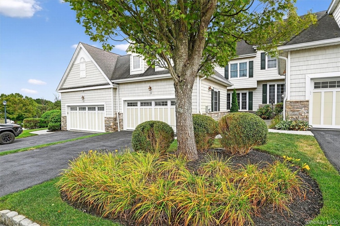 View of front of home featuring stone siding, roof with shingles, and driveway