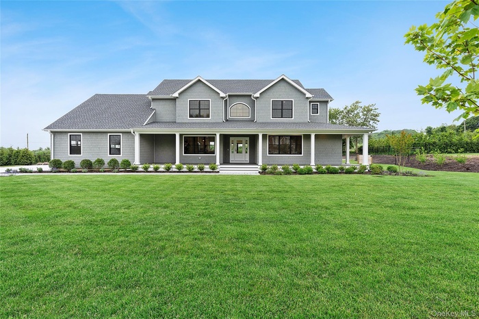 Farmhouse-style home featuring covered porch, a front yard, and a shingled roof