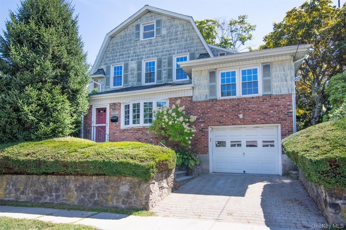 Colonial inspired home featuring a gambrel roof, an attached garage, driveway, and brick siding