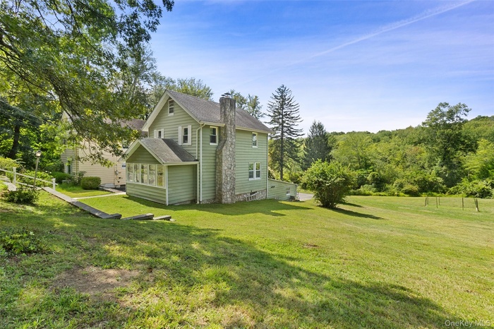 View of home's exterior featuring a yard, a sunroom, a chimney, and roof with shingles