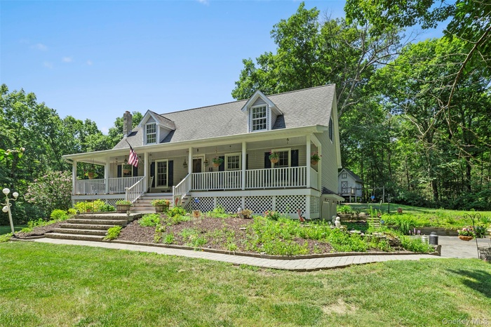 New england style home featuring covered porch, a front lawn, a shingled roof, a chimney, and stairway