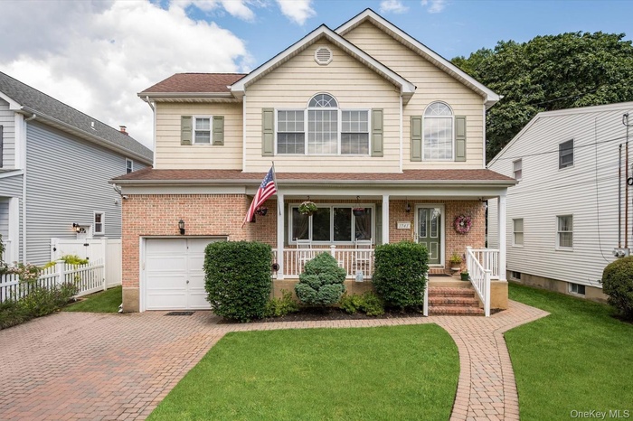 Traditional-style house with a porch, brick siding, a garage, a shingled roof, and decorative driveway