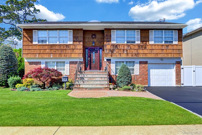 Raised ranch with brick siding, a garage, asphalt driveway, and a front lawn