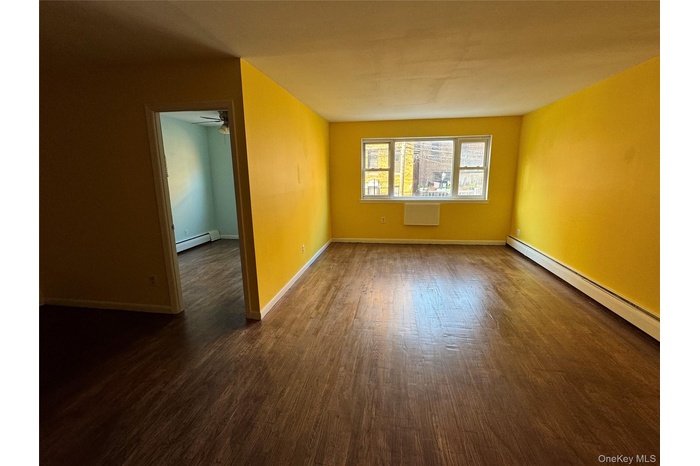 Unfurnished room featuring dark wood finished floors and baseboard heating