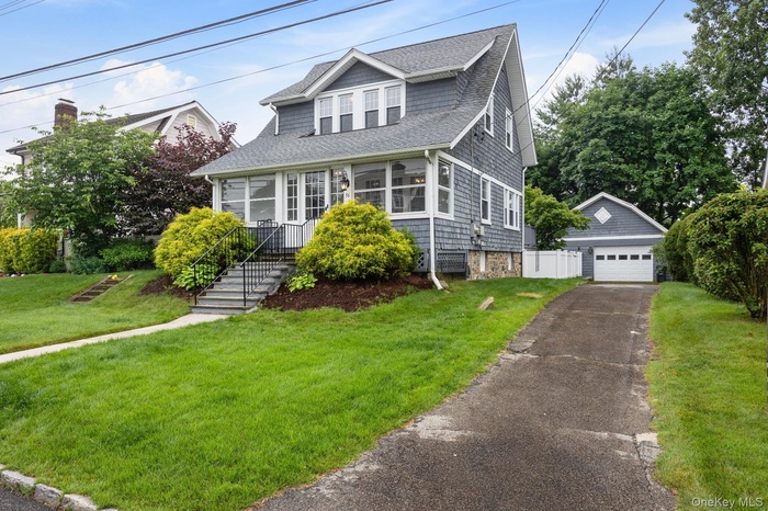 Bungalow-style house with an outdoor structure, a shingled roof, a front lawn, and a detached garage