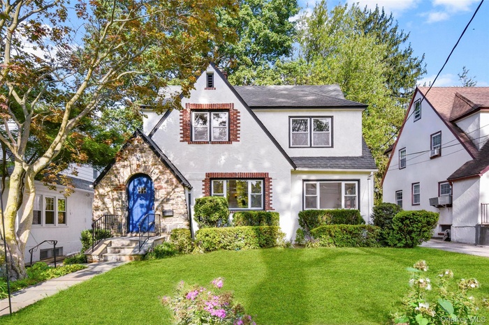 Tudor-style house featuring a front yard, stucco siding, a shingled roof, and stone siding