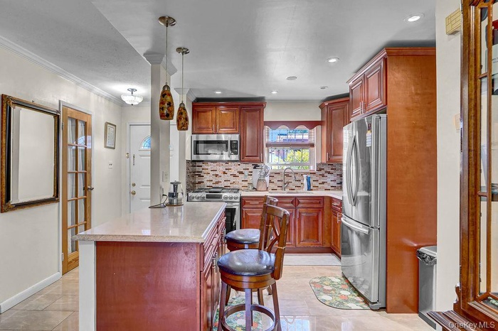 Kitchen featuring appliances with stainless steel finishes, backsplash, a kitchen island, ornamental molding, and decorative light fixtures