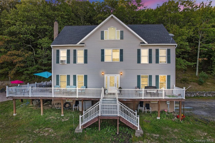 View of front of property with a wooden deck, a shingled roof, and stairs