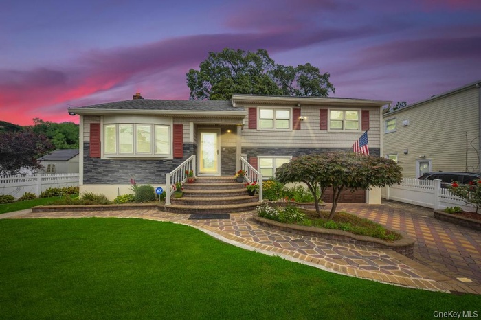 Split level home featuring stone siding, driveway, a garage, and a chimney