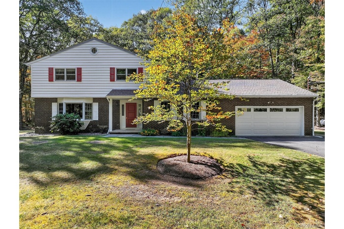 View of front of house featuring brick siding, a garage, asphalt driveway, and a front lawn