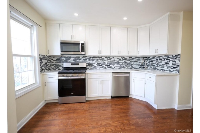 Kitchen with stainless steel appliances, white cabinetry, dark wood finished floors, decorative backsplash, and light stone counters