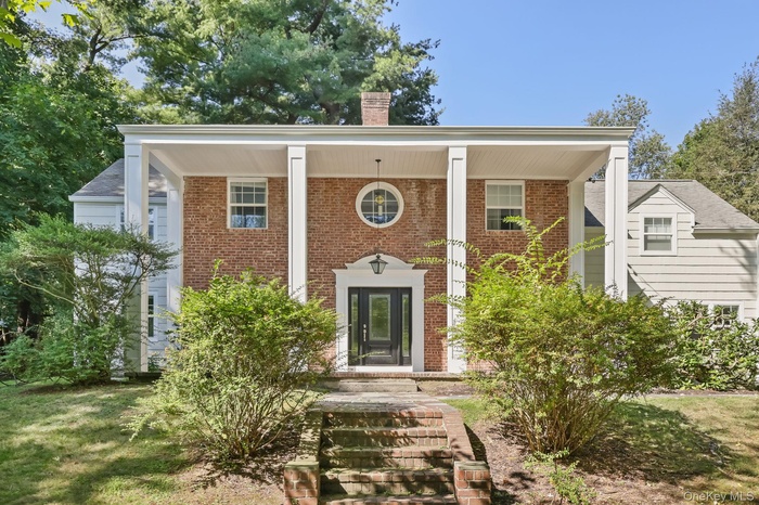 View of front of property with covered porch, a chimney, and brick siding