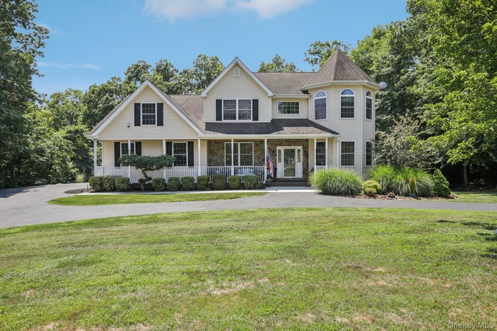 View of front of property with roof with shingles, a porch, a front lawn, stone siding, and driveway