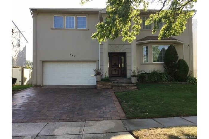 View of front of property featuring a garage, stucco siding, decorative driveway, and a front yard