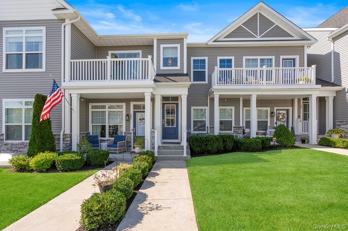 View of front of home with a front yard, a balcony, and stone siding